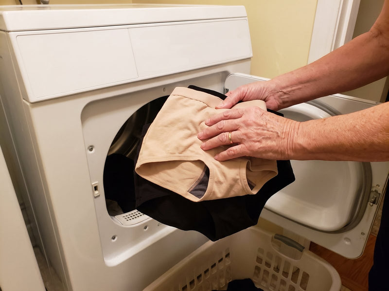 An older woman lifts a clean beige and black pair of Haven underwear out of a tumble dryer